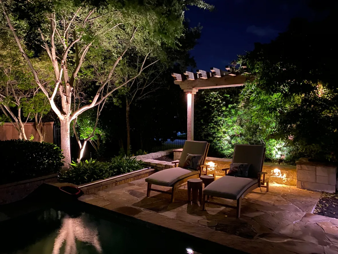 Pool and lounge seating at night with the surrounding planting and structures softly lit