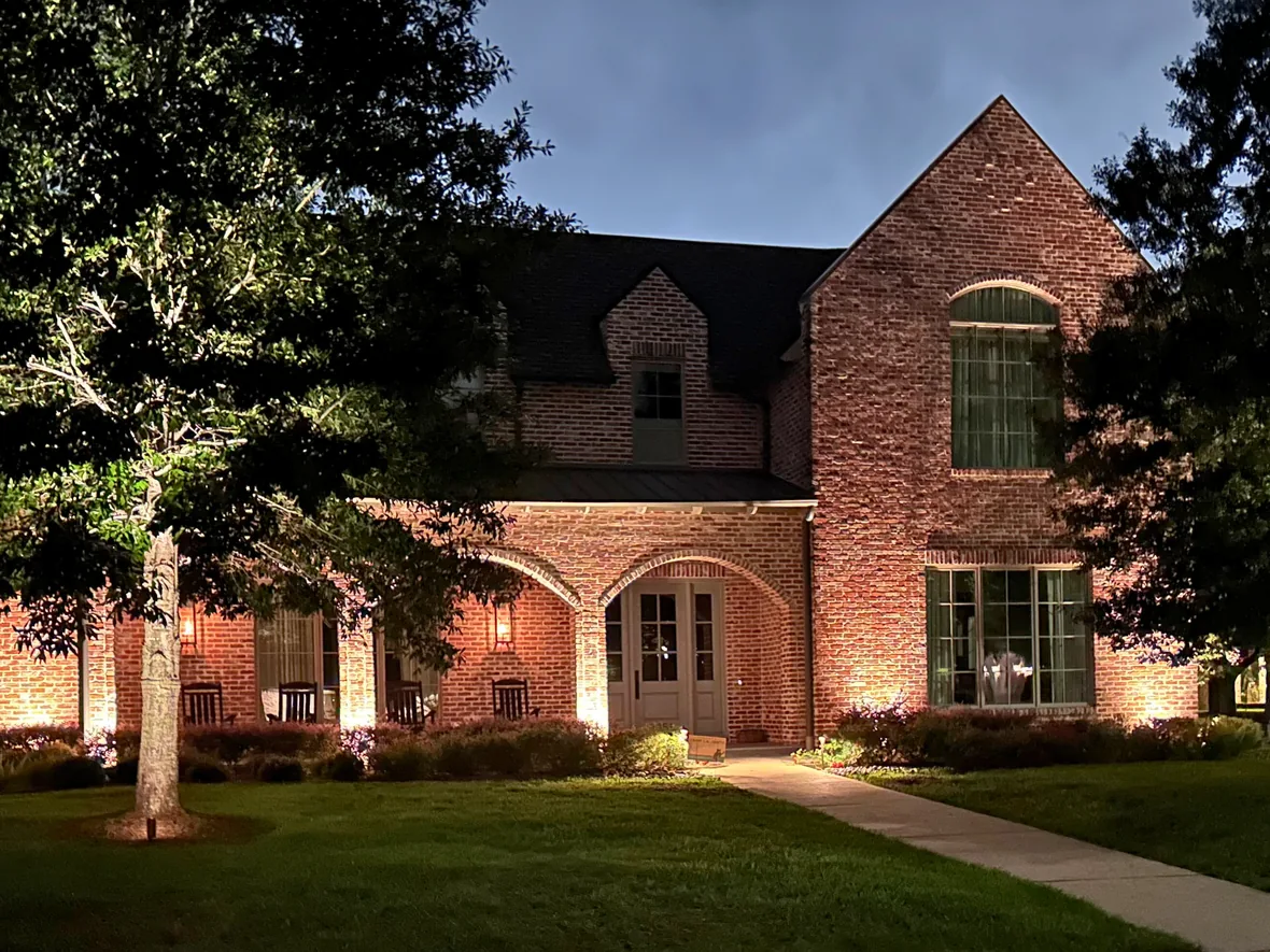 Brick home at dusk with an uplit oak in the front lawn and a lit walkway to the entry