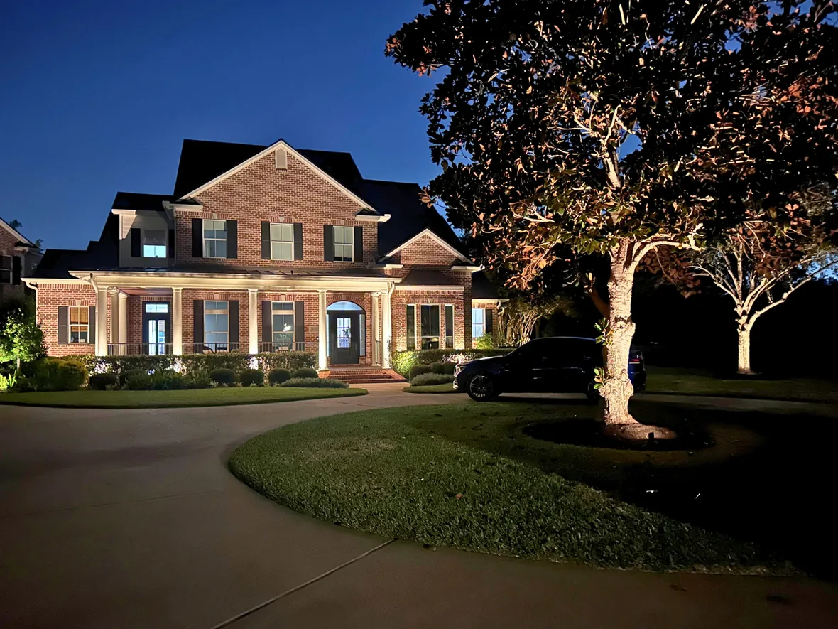 Stone facade and landscaping lit with low-voltage brass fixtures hidden in the planting beds
